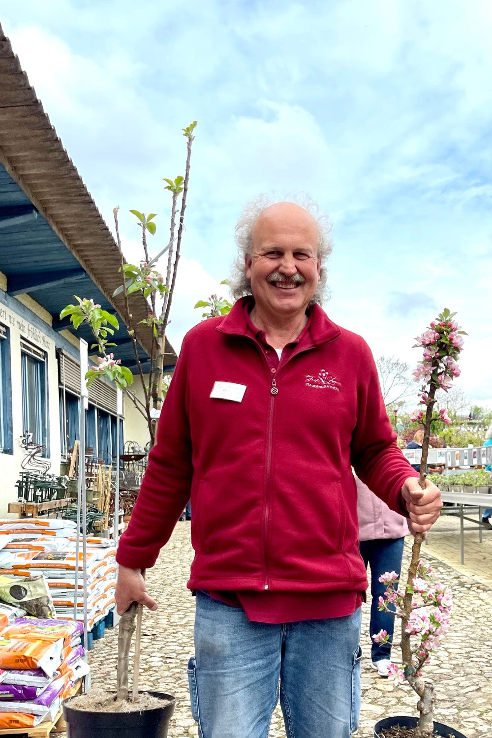 Gärtner trägt am Gartenfest zwei Obstbäume